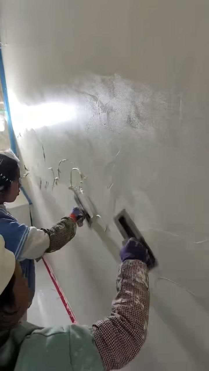 Two CALMURA application advisers troweling microcement onto a hotel wall in real time — photographed during the 11-week finish phase