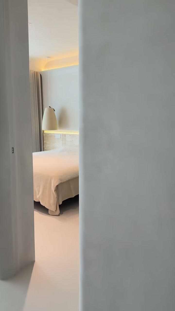 Hotel guest bedroom finished in continuous microcement — wall, ceiling and floor read as a single plane, integrated cove lighting behind the bedhead