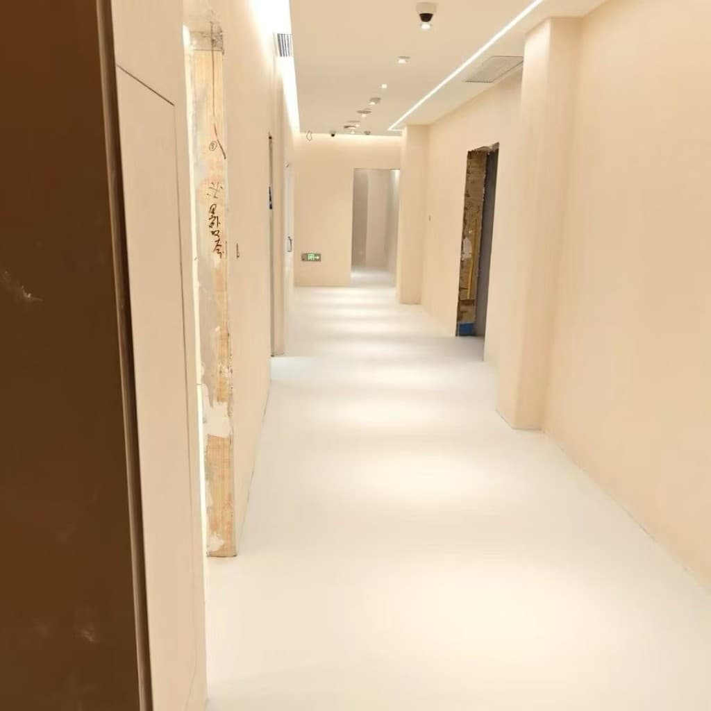 Long view down a hotel corridor finished in peach-cream limewash and microcement floor, doors recessed into the wall