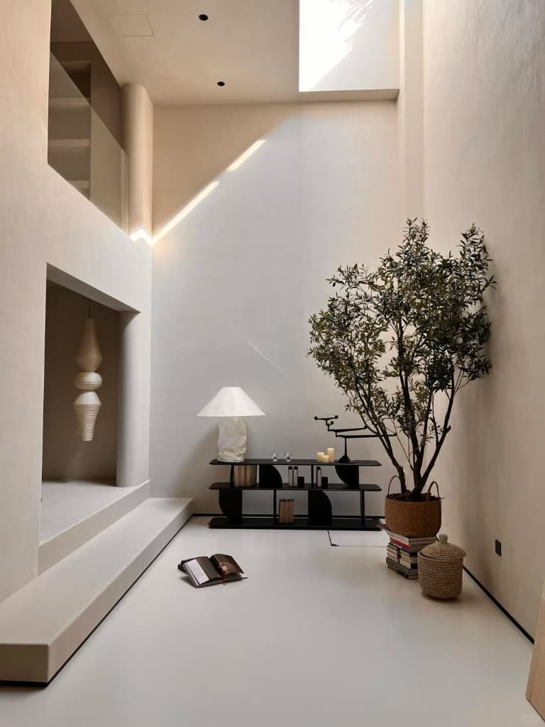 Double-height private villa entry finished in warm cream marmorino on every wall and a continuous microcement floor, with a sculpted niche and rattan pendant lights